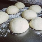 Close-up of fresh dough balls on a floured surface, ready for baking.